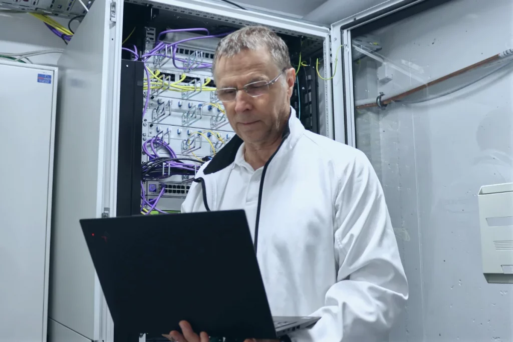 Thomas Spreitzer von TSE Services prüft Daten auf seinem Laptop vor einem offenen Serverschrank.
